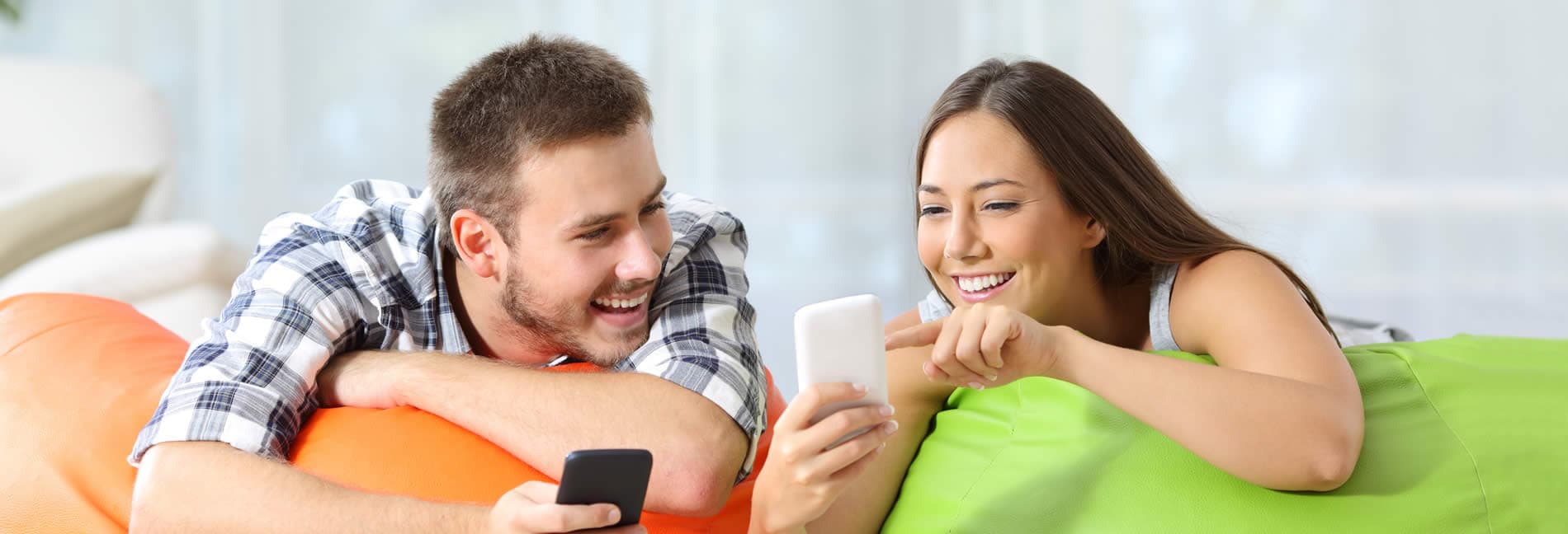 Smiling young woman points out something on her smartphone screen to young man who is also holding a smartphone